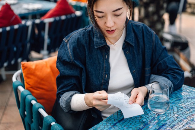 Young Asian woman reviewing the bills at the outdoor restaurant. Bills and payment concepts