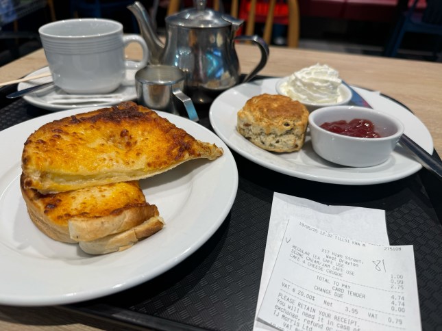 A tray of food on a table at Home Bargains cafe, with a cheese toastie, scone with cream and jam and a pot of tea