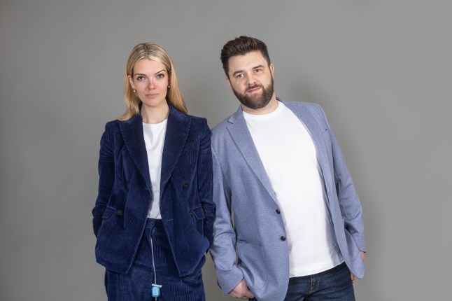 Celia Chartres-Aris and Jamie Shields in smart businesswear in a blue shade. They are stood in front of a grey background