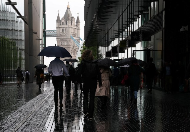 Workers shield from the rain as they walk near Tower Bridge during the morning rush-hour, in London, Britain, May 21, 2025. REUTERS/Toby Melville